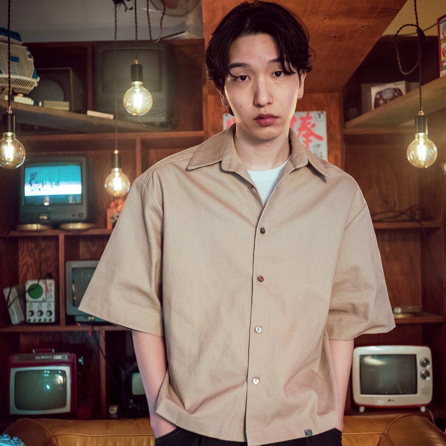 Person wearing a beige shirt in a room with vintage TVs and lighting fixtures.