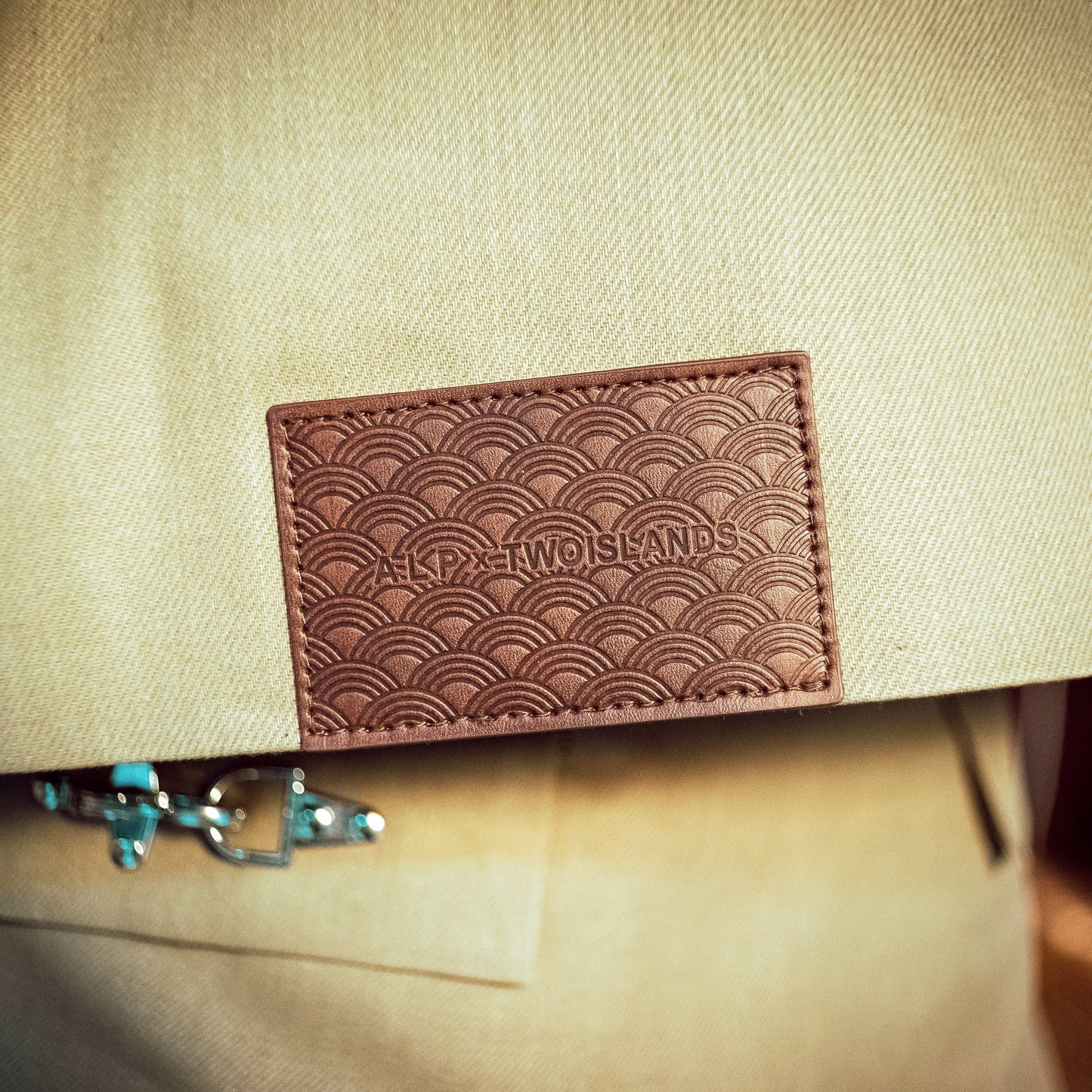 Beige fabric with a brown leather patch featuring embossed text.