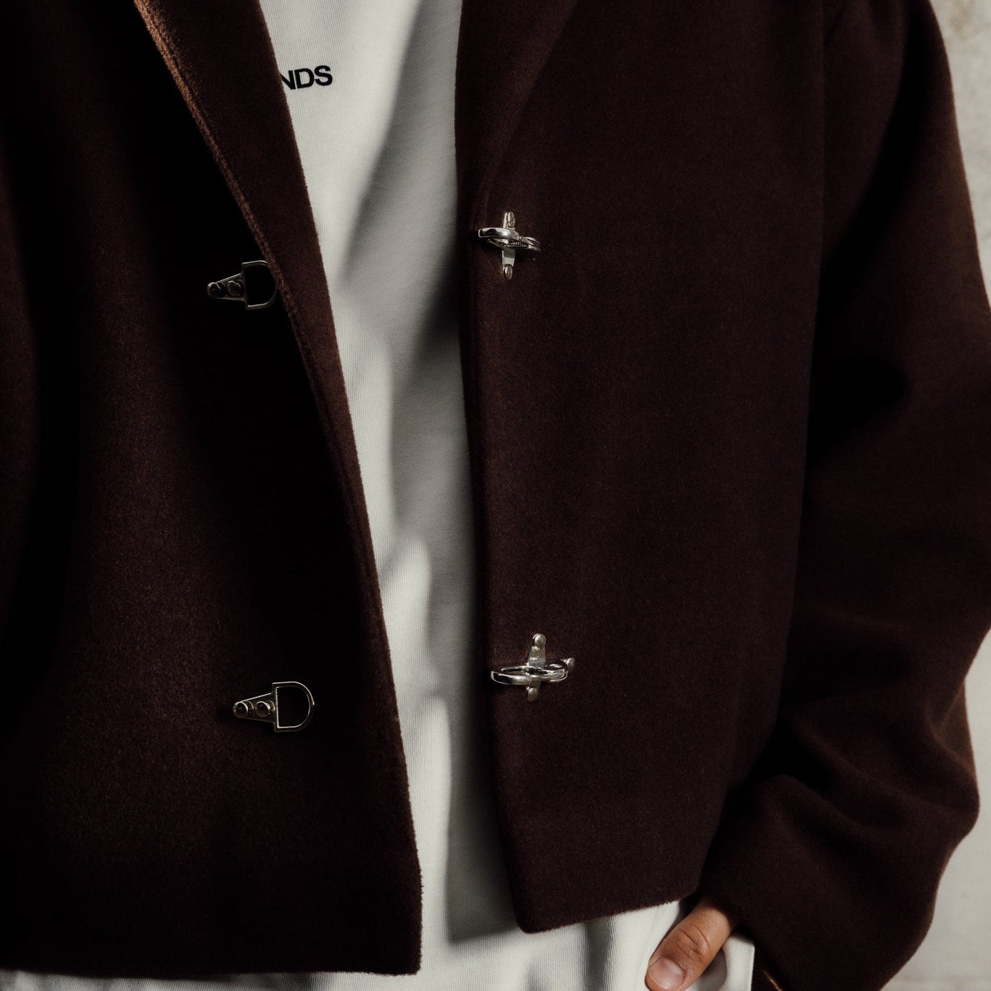 Brown coat with silver buttons over a white shirt against a neutral background