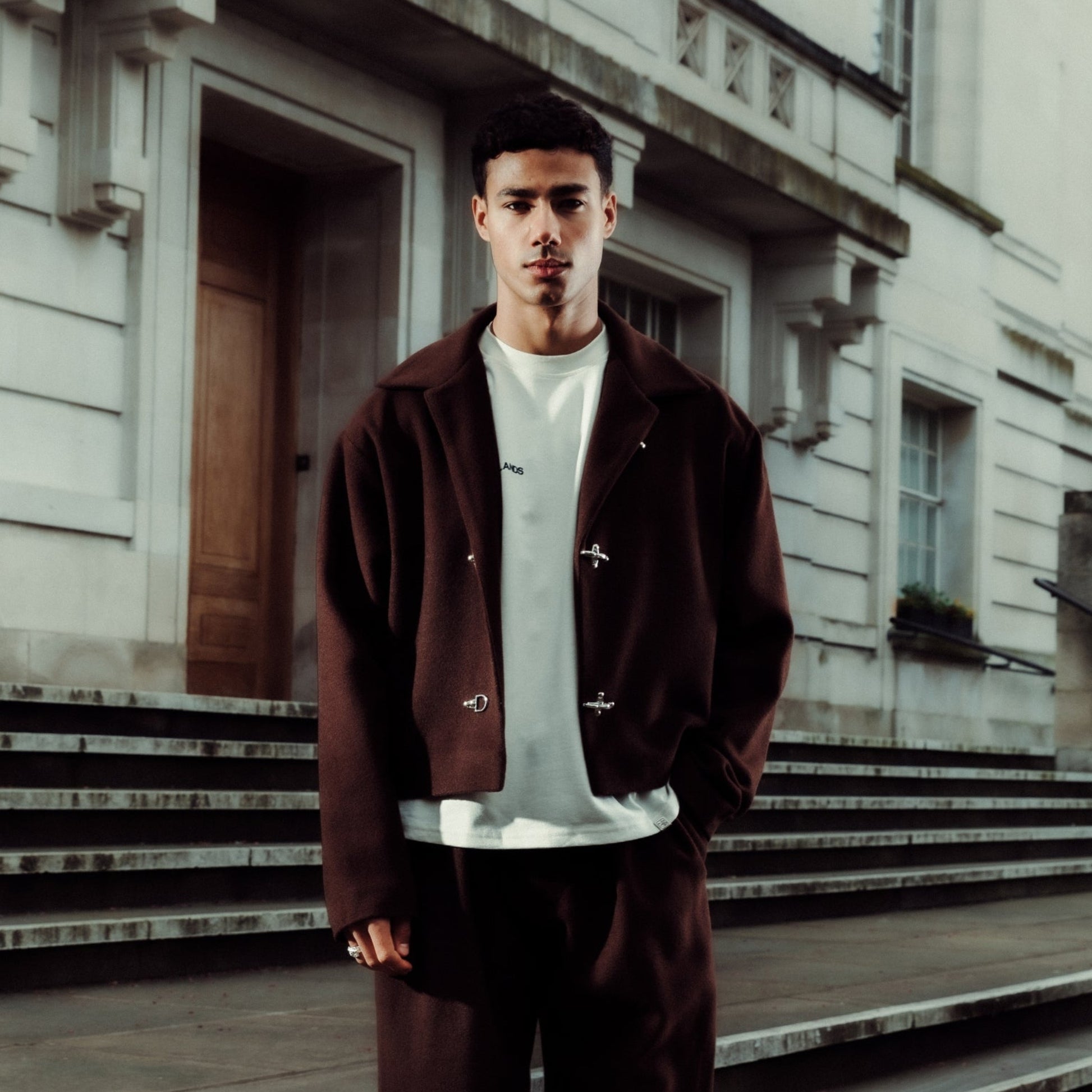 Man in a brown tracksuit standing on stone steps in front of a building