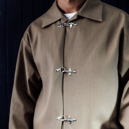 Person wearing akhaki jacket with metal buttons against a dark background