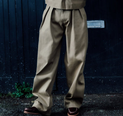 Person wearing a khaki outfit standing against a dark blue wall.