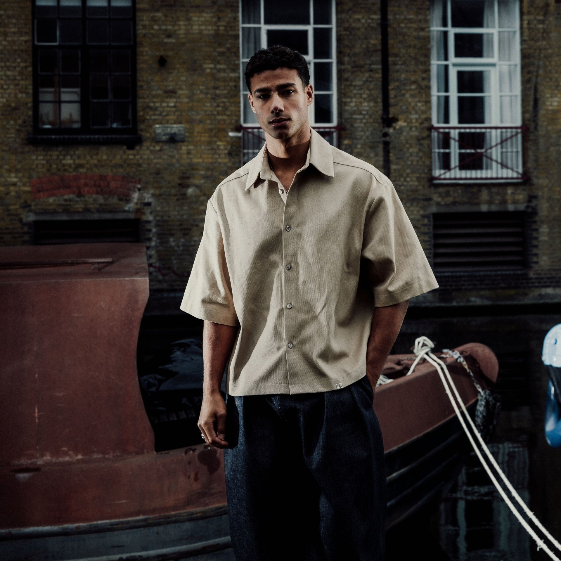 Man standing in front of a brick building with windows in cream oversized shirt