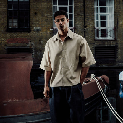 Man standing in front of a brick building with windows in cream oversized shirt