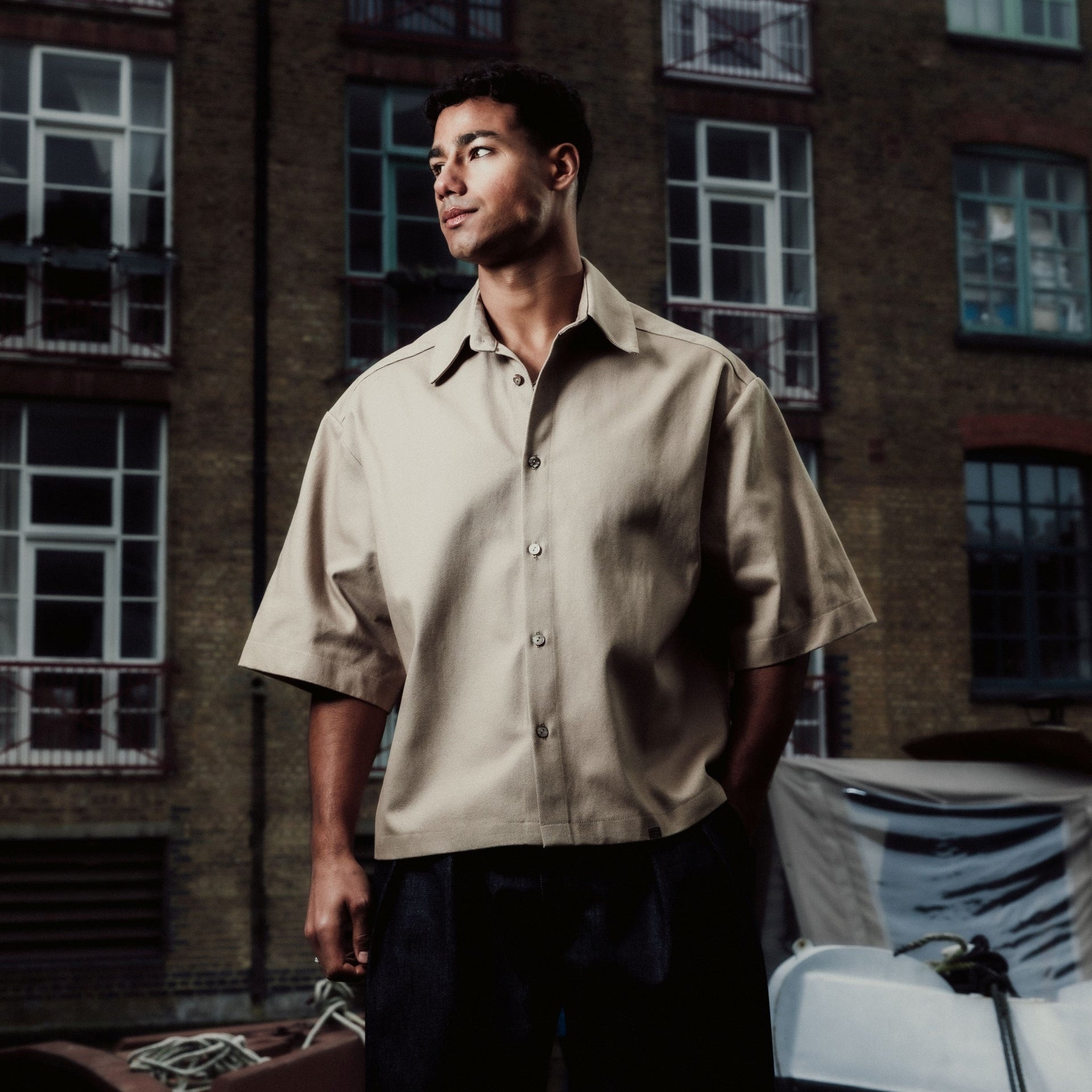 Man standing by a boat in an urban setting with a building in the background